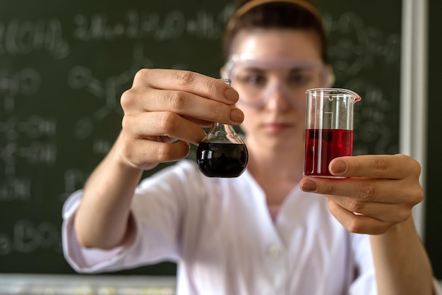 cientista feminina fazendo testes científicos com frasco químico e líquido no laboratório da escola