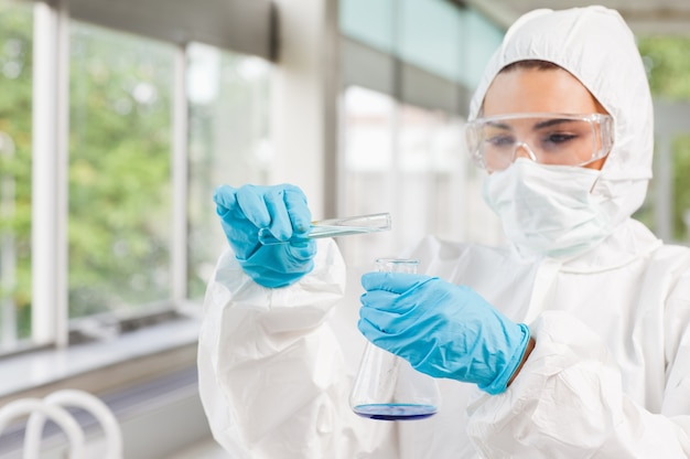 Cientista feminino protegido que despeja líquido