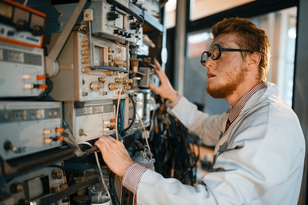 Cientista louco de óculos ajusta dispositivo elétrico em laboratório.