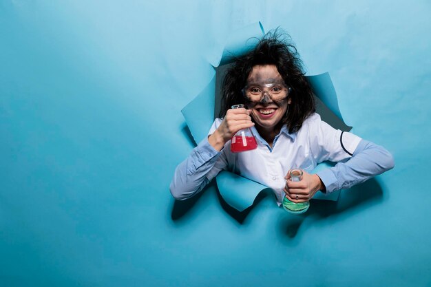 Cientista louco louco com frascos de vidro cheios de compostos químicos. Químico insano com expressão facial boba segurando frascos de vidro cheios de soro líquido experimental enquanto olha para a câmera.