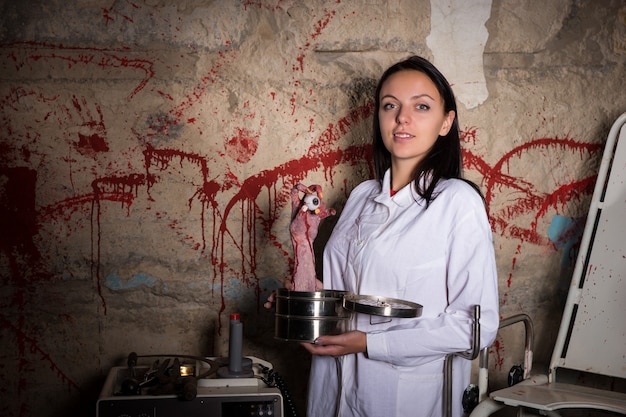 Cientista maluca segurando uma mão decepada e um globo ocular em uma caixa em frente a uma parede respingada de sangue, conceito de Halloween