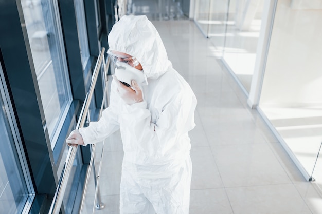 Cientista médica no jaleco, óculos de proteção e máscara em pé dentro de casa
