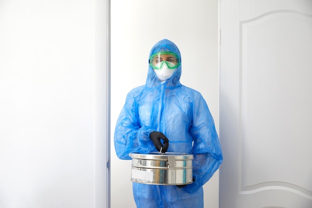 Cientista médico irreconhecível em uniforme de proteção, abrindo portas e entrando na sala do laboratório segurando uma caixa de metal com amostras.