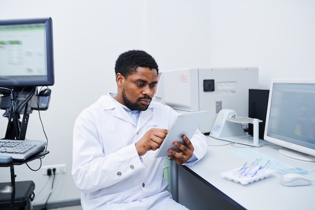 Cientista médico preto, analisando dados sobre tablet