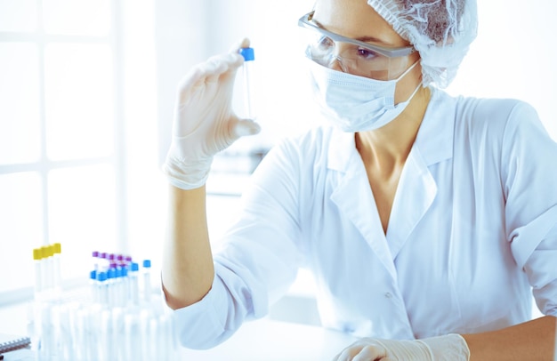 Cientista profissional em óculos de proteção pesquisando tubo com reagentes em laboratório ensolarado em tons de azul Medicina e pesquisa científica