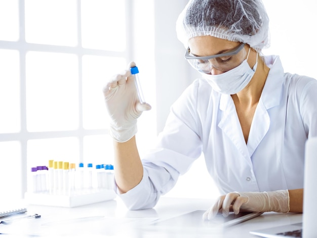 Cientista profissional feminina em óculos de proteção, pesquisando tubo com reagentes em laboratório. Conceitos de medicina e pesquisa científica.