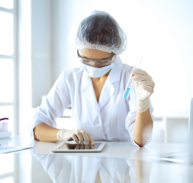 Cientista profissional feminina em óculos de proteção, pesquisando tubo com reagentes em laboratório. Conceitos de medicina e pesquisa.