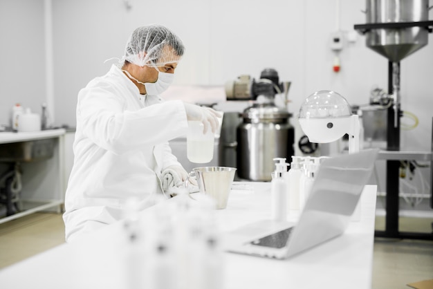 Cientista profissional moderno, sentado à mesa com toalha e balão no laboratório de tecidos cosméticos