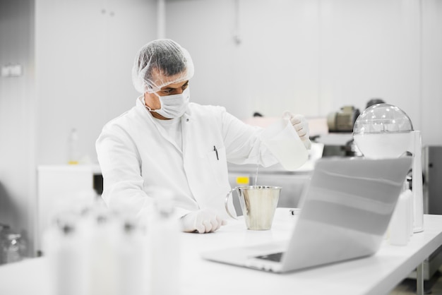 Cientista profissional moderno, sentado à mesa e derramar líquido de um balão para outro no laboratório de tecidos cosméticos