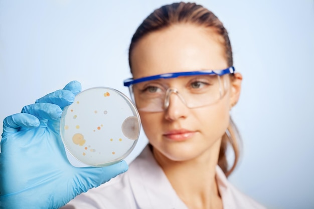 Foto cientista ruiva olha de perto a placa de petri com alguma bactéria nela,