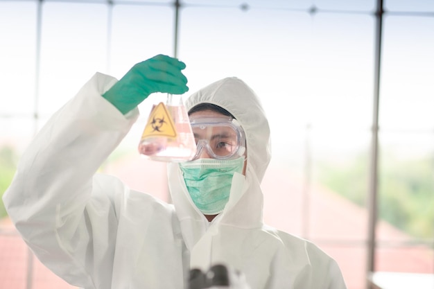 Foto cientista vestindo fato de proteção segurando um frasco no laboratório