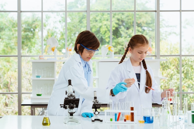 Cientistas de duas crianças fazendo experimentos químicos com microscópio na sala do laboratório.
