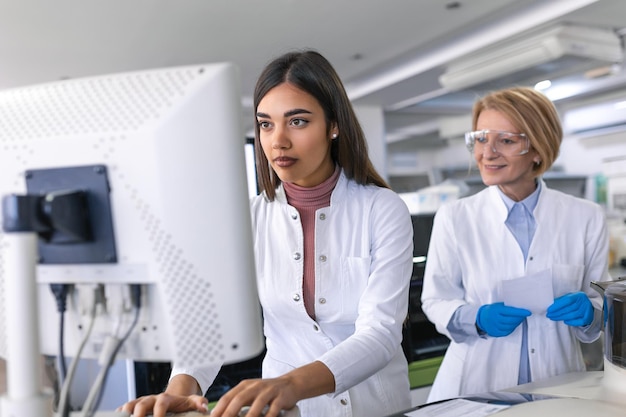 Foto cientistas femininas programam equipamento médico com computador pessoal equipe de profissionais trabalhando em laboratório moderno de pesquisa farmacêutica