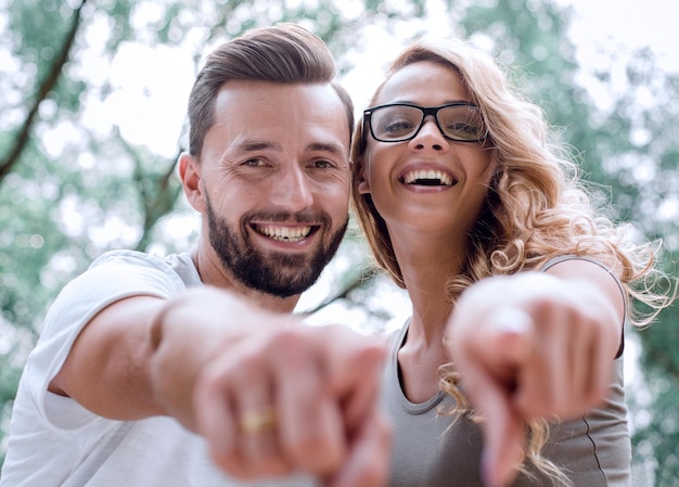 Cierra a felices recién casados parados en el parque y señalando tu foto con espacio de copia