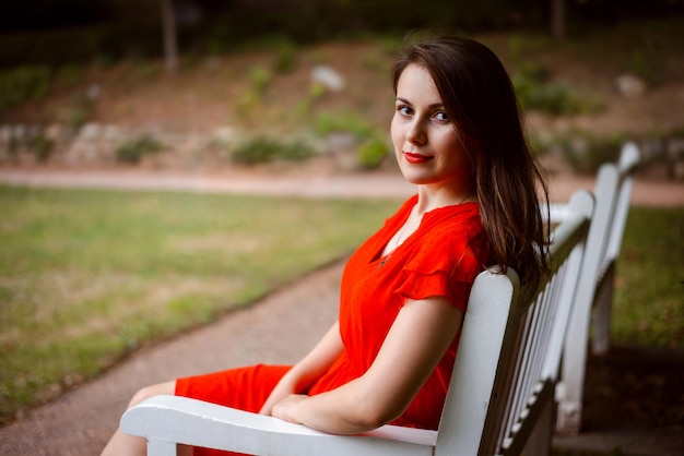 Cierra la foto de una hermosa chica vestida de rojo sentada en un banco blanco