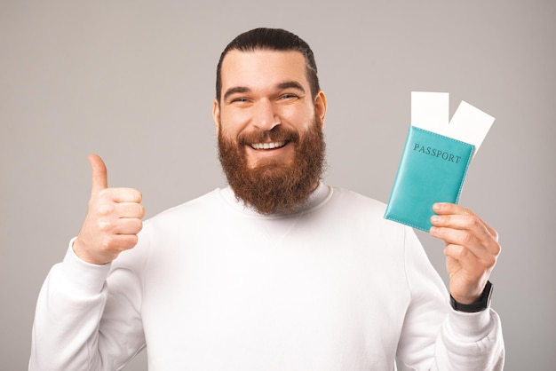 Cierra la foto de un hombre barbudo que muestra el pulgar hacia arriba mientras sostiene un pasaporte