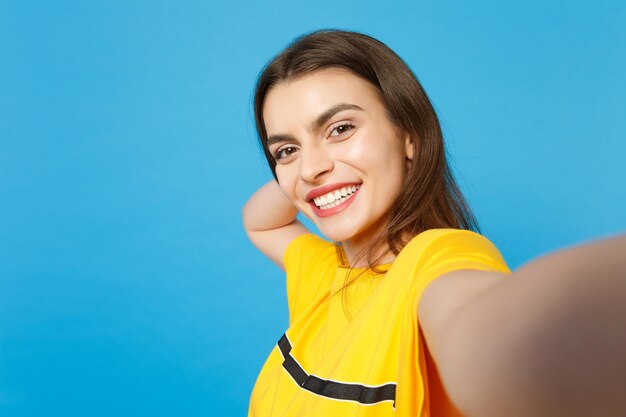 Cierra la foto selfie de una mujer joven hermosa y atractiva sonriente con ropa casual vívida mirando una cámara aislada en un fondo de pared azul brillante en el estudio. Concepto de estilo de vida de las personas. Simulacros de espacio de copia.