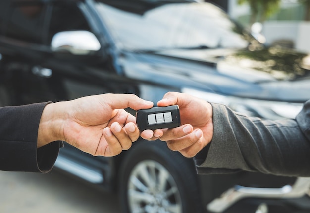 Cierra a un hombre de negocios en traje con las manos mostrando o dando la llave del auto para que el cliente obtenga un auto nuevo. Comprar vender alquiler concepto de coche.