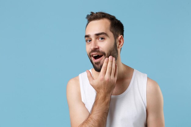 Cierra a un joven barbudo de 20 años de edad con una piel perfecta y una camisa blanca aislada en un fondo de pared azul pastel, retrato de estudio. Concepto de procedimientos cosméticos para el cuidado de la piel. Simulacros de espacio de copia