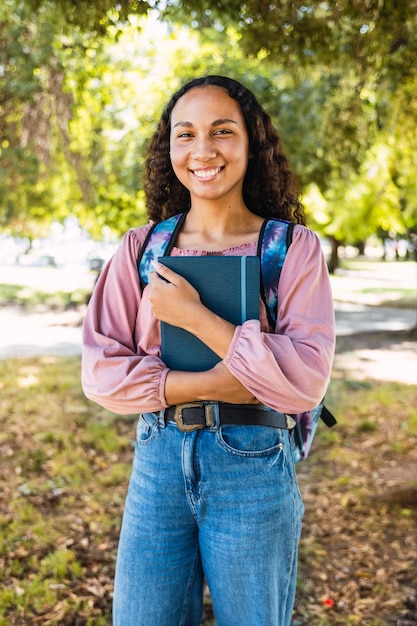 Cierra a una joven estudiante latina feliz sosteniendo sus libros en el parque. Autoconfianza saludable