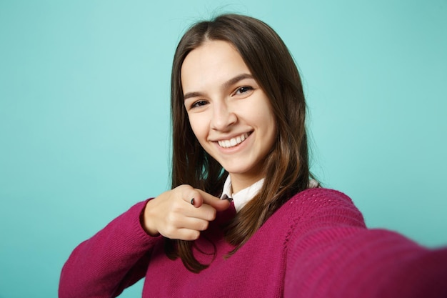 Cierra a una joven morena con ropa informal posando haciendo selfie en un teléfono móvil aislado en un retrato de estudio de fondo azul. Gente emociones sinceras concepto de estilo de vida. Simulacros de espacio de copia