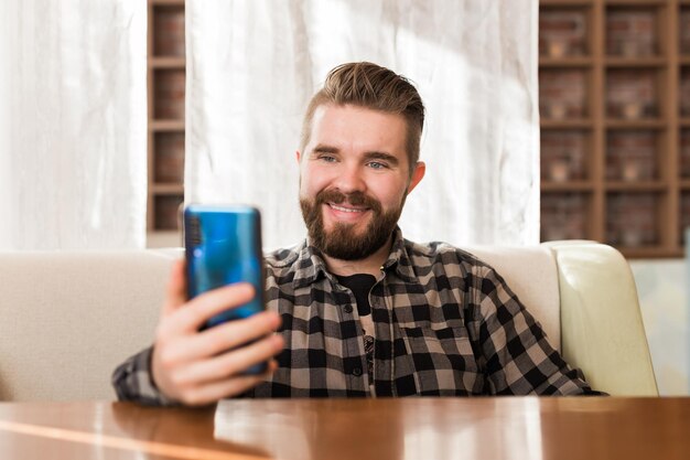 Cierra a un joven sentado en una cafetería y usa una videollamada desde un teléfono inteligente para saludar y hablar con amigos y familiares para un nuevo concepto de estilo de vida normal y saludable