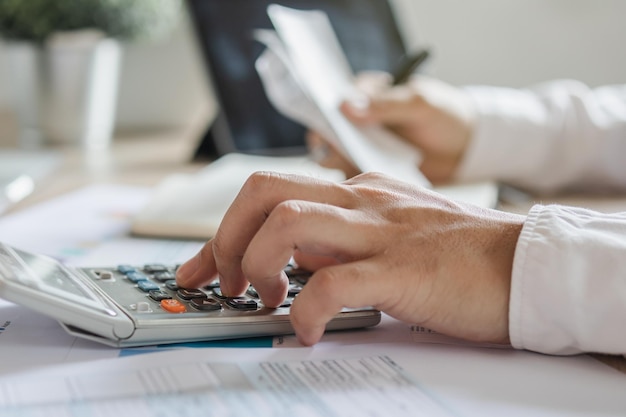 Cierra la mano de un joven hombre de negocios asiático que presiona la calculadora para calcular los ingresos y gastos fiscales de la tarjeta de crédito para el pago o el día de pago en la oficina en casa Concepto de finanzas financieras