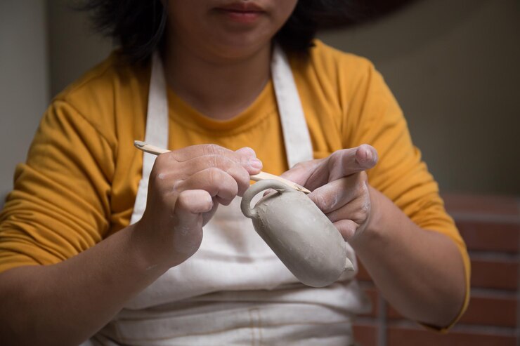 Foto cierra la mano de una mujer asiática usando una rueda de cerámica para hacer una tetera en el taller