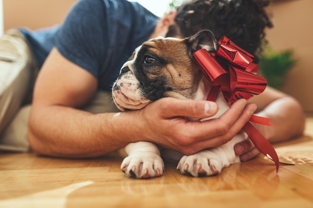 Cierra las manos de un joven que está acostado en el suelo y abrazando a su pequeño cachorro después de que trajo cajas con cosas a su nuevo hogar.