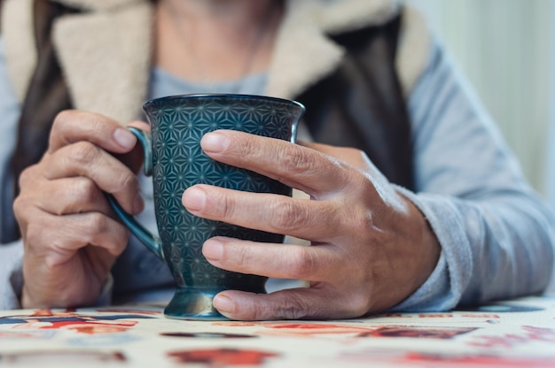 Cierra las manos de una mujer adulta sosteniendo una taza de porcelana en la mesa