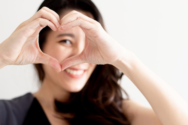 Cierra a una mujer hermosa asiática haciendo un símbolo en forma de corazón a mano frente a su cara. Un día de San Valentín y amor