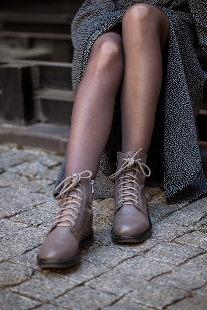 Cierra las piernas de una mujer con un vestido elegante y zapatos de cuero informales sentados en las escaleras de la calle