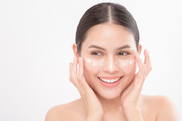 Cierra el retrato de belleza de una joven hermosa mujer sonriente aplicando crema facial