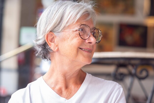 Cierra el retrato de una hermosa anciana caucásica con el pelo corto blanco y anteojos mirando dentro del restaurante mientras está sentada