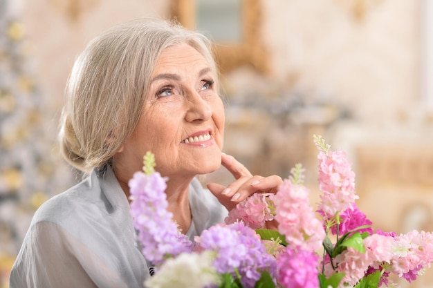 Cierra el retrato de una hermosa anciana posando en casa con flores.
