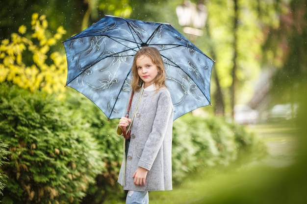 Cierra el retrato de una hermosa y elegante niña con un paraguas bajo la lluvia en el parque