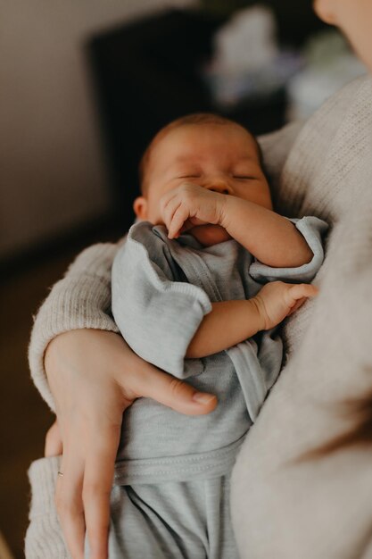 Cierra el retrato de un hermoso bebé dormido en los brazos de mamá en el dormitorio a la luz del día