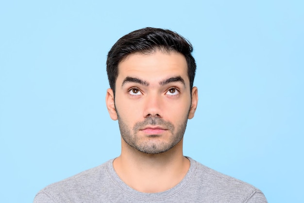 Foto cierra el retrato de un hombre caucásico guapo y serio que piensa mientras mira hacia arriba en un estudio aislado de fondo azul.