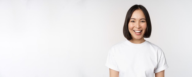 Cierra el retrato de una joven asiática mirando a la cámara con una camiseta sonriendo y con un fondo blanco feliz