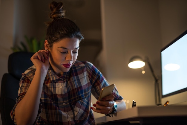 Cierra el retrato de una joven empresaria que usa un teléfono móvil en la oficina en el trabajo nocturno.