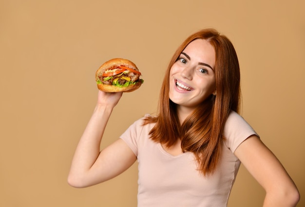 Cierra el retrato de una joven hambrienta comiendo hamburguesas aislada sobre un fondo desnudo