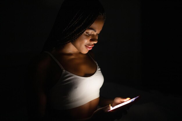 Cierra el retrato de una mujer afroamericana mirando el teléfono mientras está en la cama.