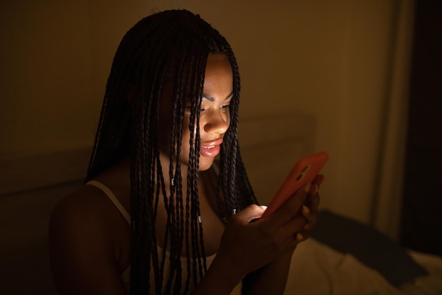 Cierra el retrato de una mujer afroamericana mirando el teléfono mientras está en la cama.