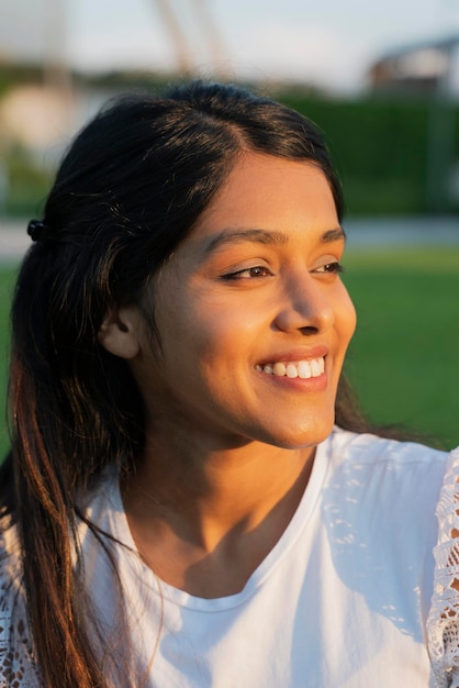 Cierra el retrato de una mujer india feliz mirando hacia otro lado sentada en el parque. concepto de verano