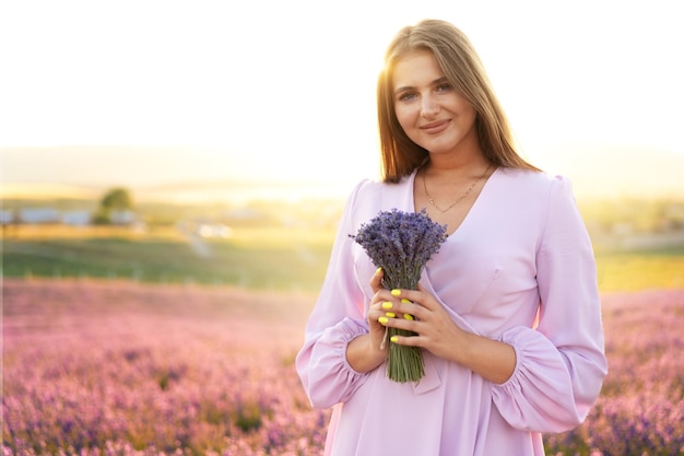 Cierra el retrato de una mujer joven sosteniendo un ramo de lavanda mientras está de pie en un campo de lavanda