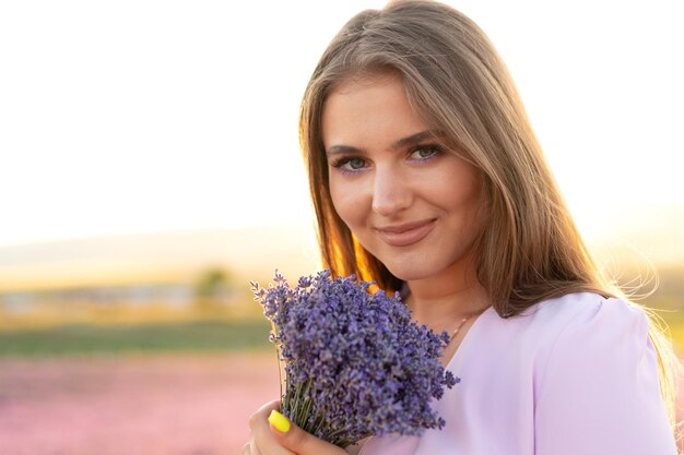 Cierra el retrato de una mujer joven sosteniendo un ramo de lavanda mientras está de pie en un campo de lavanda