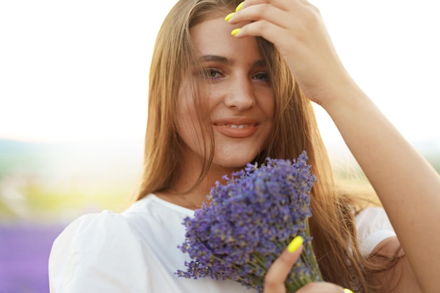 Cierra el retrato de una mujer joven sosteniendo un ramo de lavanda mientras está de pie en un campo de lavanda