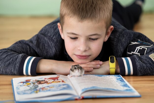 Cierra el retrato de un niño pequeño sonriente leyendo un libro con pequeños hámsteres. Concepto de estudiar con buen humor.