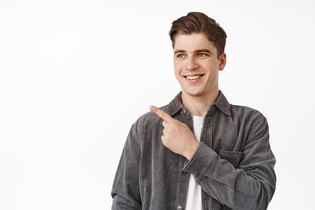 Cierra el retrato de un universitario sonriente, estudiante señalando y mirando a la izquierda con cara feliz, mostrando el logo de la pancarta, publicidad en el espacio vacío, fondo blanco