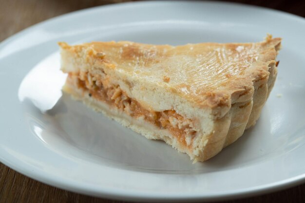 Cierra un trozo de pastel de pollo con requesón, tomates, cebolla y aceitunas sobre una mesa de madera y un plato blanco